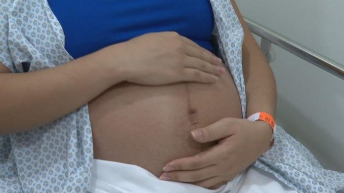 com-roupa-de-hospital-mulher-na-reta-final-da-gravidez-coloca-a-mao-na-barriga